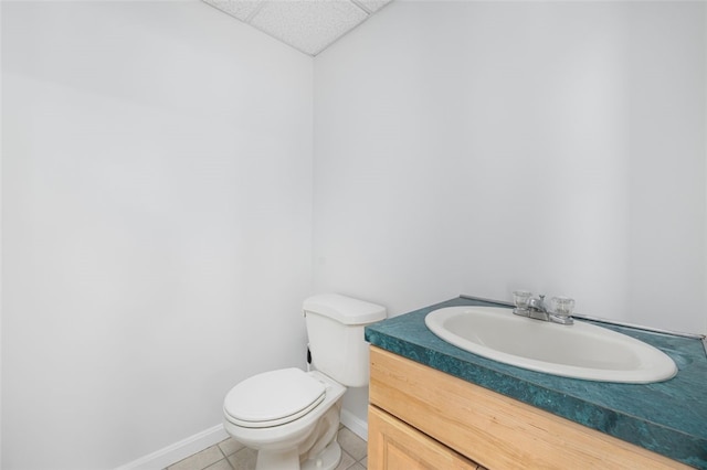 half bath featuring toilet, a drop ceiling, tile patterned flooring, baseboards, and vanity