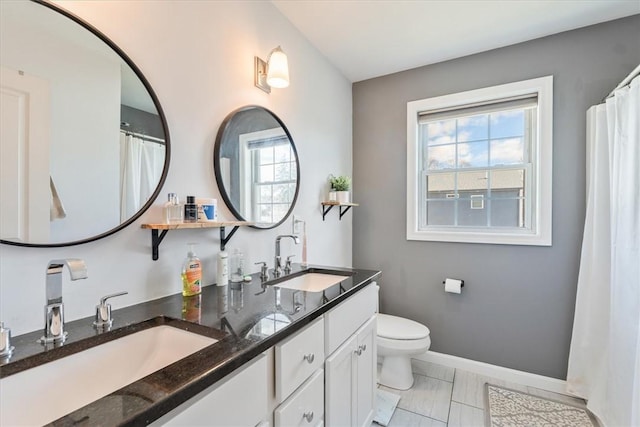 bathroom with double vanity, toilet, baseboards, and a sink