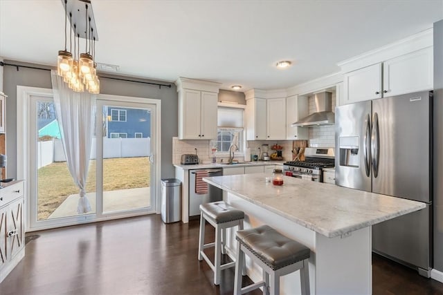 kitchen featuring wall chimney range hood, decorative backsplash, a kitchen breakfast bar, appliances with stainless steel finishes, and a sink