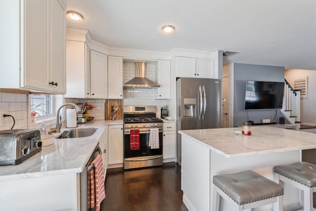 kitchen with tasteful backsplash, appliances with stainless steel finishes, white cabinetry, wall chimney exhaust hood, and a sink