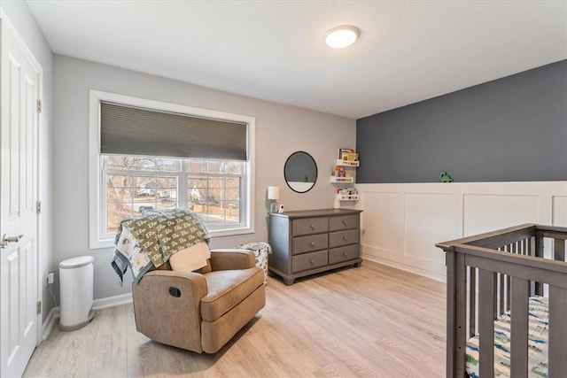 bedroom with a decorative wall, a nursery area, light wood-style floors, and a wainscoted wall