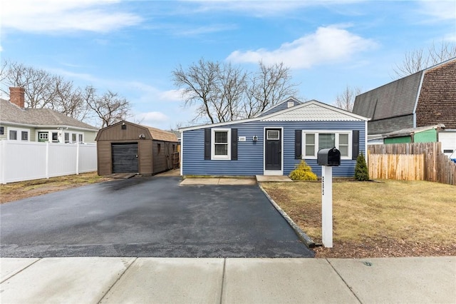 view of front facade featuring a front yard, an outbuilding, fence, a storage unit, and aphalt driveway