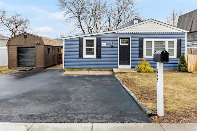 view of front facade with a front lawn, aphalt driveway, fence, a storage shed, and an outdoor structure