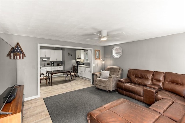 living room featuring ceiling fan, baseboards, and light wood-style flooring