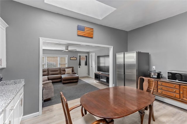 dining space with a skylight, light wood-style floors, baseboards, and ceiling fan