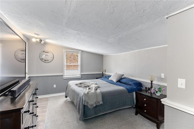 bedroom featuring vaulted ceiling, light wood-style flooring, a wainscoted wall, and a textured ceiling