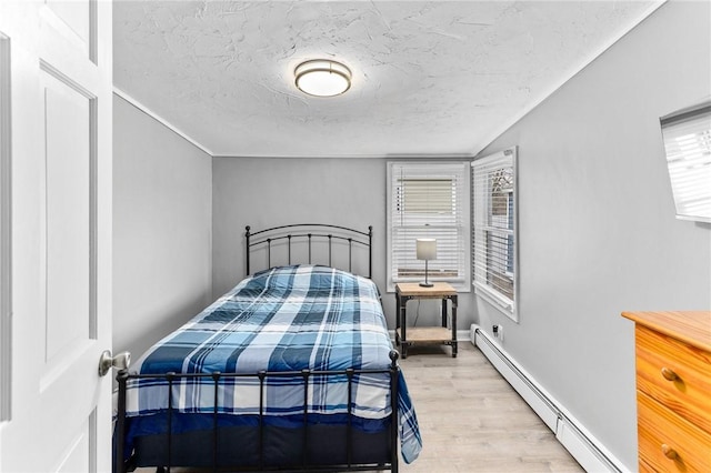 bedroom featuring light wood-style floors, baseboards, baseboard heating, and a textured ceiling