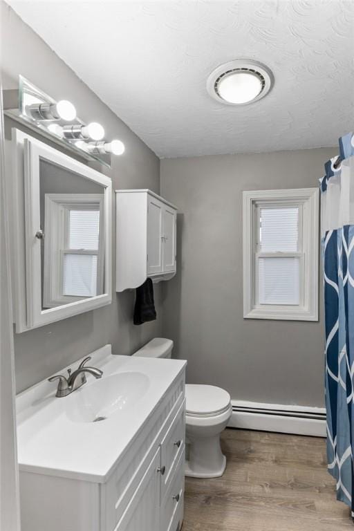 full bathroom featuring vanity, wood finished floors, a textured ceiling, a baseboard heating unit, and toilet