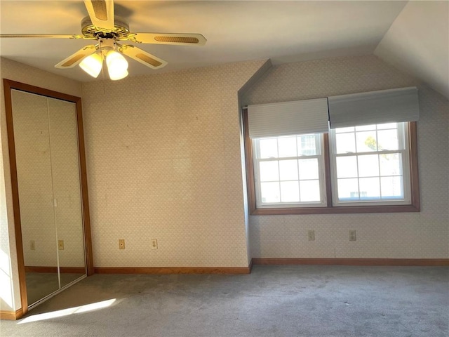 unfurnished bedroom featuring a closet, wallpapered walls, lofted ceiling, and carpet