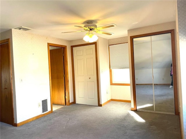 unfurnished bedroom with visible vents, multiple closets, carpet floors, and wallpapered walls