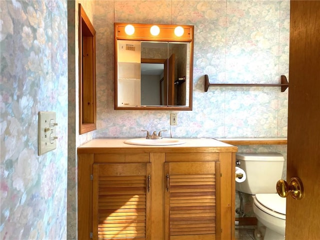 bathroom with toilet, vanity, and wallpapered walls