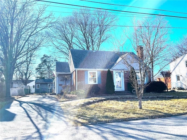 view of front of property featuring brick siding, roof with shingles, and a chimney