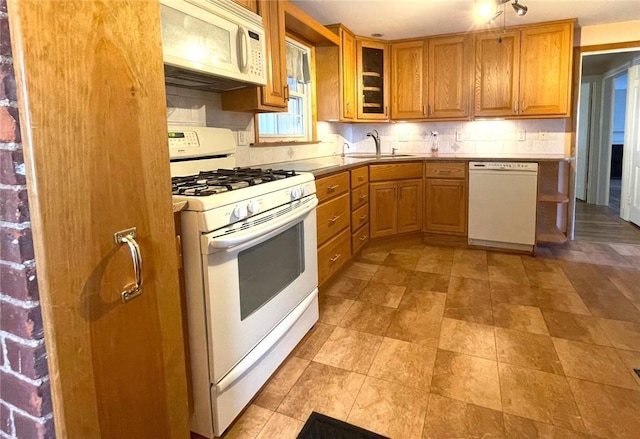 kitchen with decorative backsplash, a sink, white appliances, brown cabinetry, and glass insert cabinets