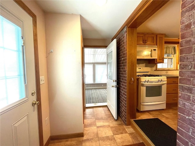 kitchen with white appliances, brown cabinetry, baseboards, and brick wall