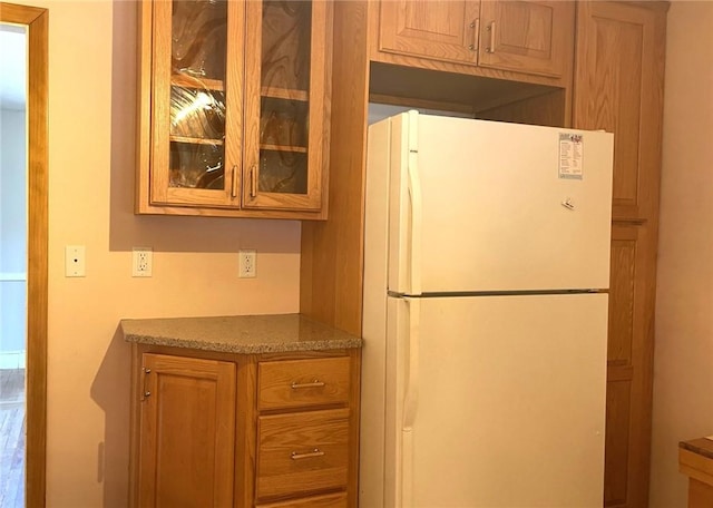 kitchen featuring glass insert cabinets, brown cabinets, and freestanding refrigerator