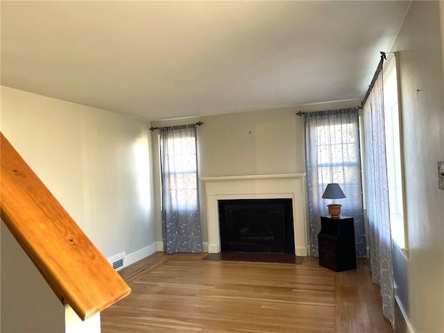 unfurnished living room with a fireplace with flush hearth, baseboards, visible vents, and wood finished floors