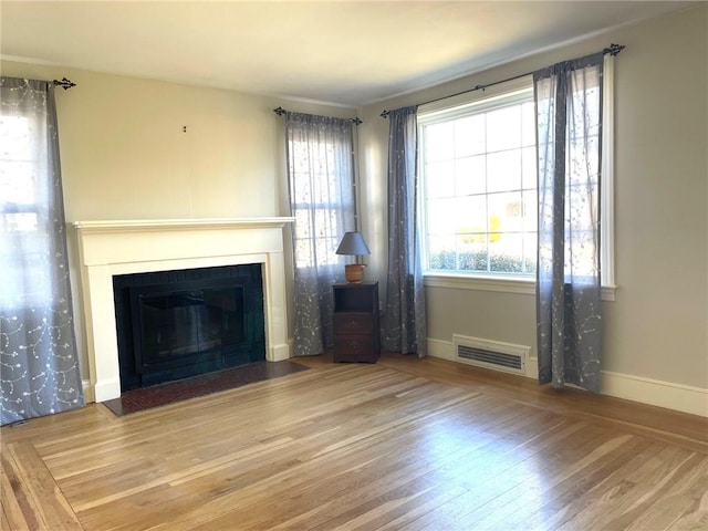 unfurnished living room featuring visible vents, baseboards, a fireplace with flush hearth, and wood finished floors