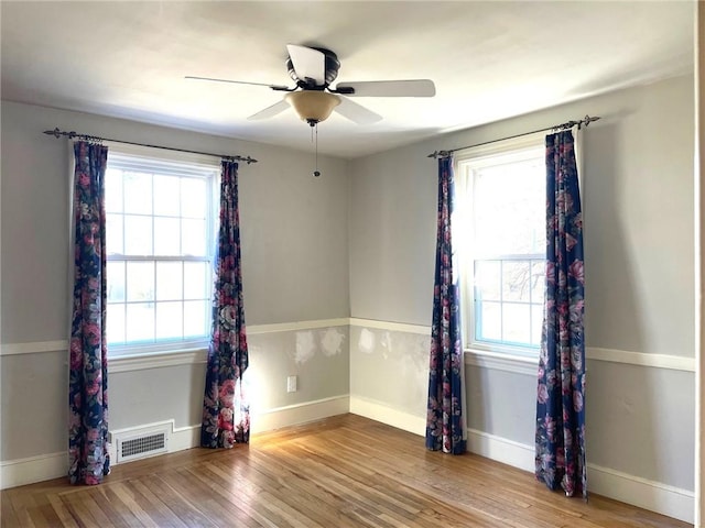 empty room featuring ceiling fan, visible vents, baseboards, and wood finished floors