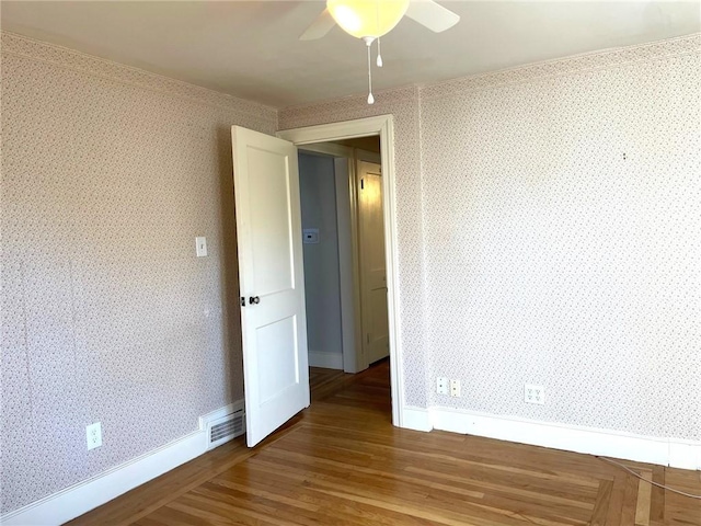 spare room featuring visible vents, wallpapered walls, baseboards, wood finished floors, and a ceiling fan