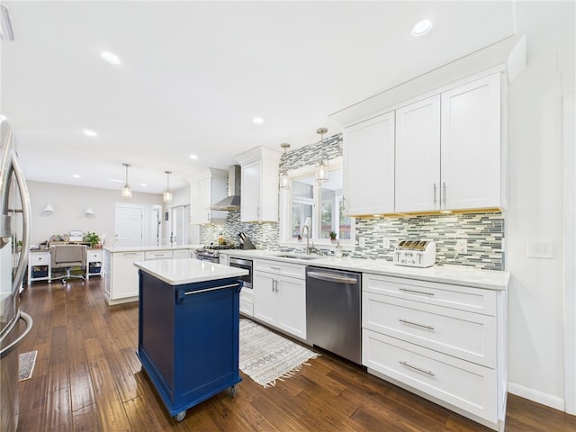 kitchen with a peninsula, a sink, decorative backsplash, appliances with stainless steel finishes, and wall chimney exhaust hood