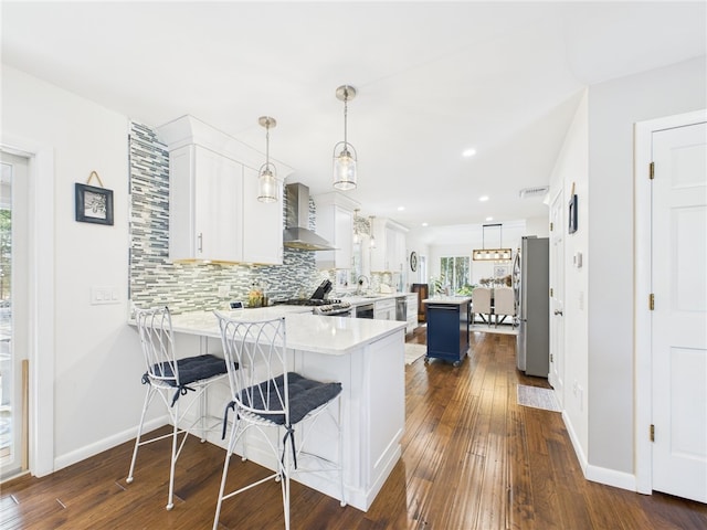 kitchen featuring backsplash, freestanding refrigerator, a peninsula, wall chimney exhaust hood, and light countertops