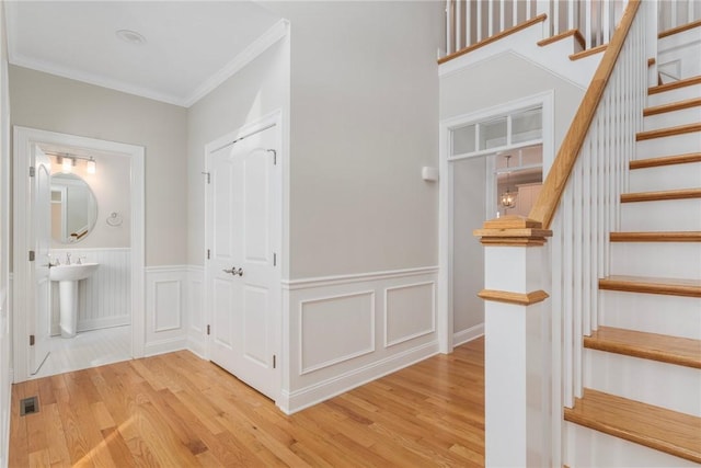 stairway with visible vents, wood finished floors, wainscoting, and ornamental molding