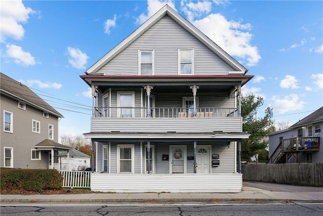 view of front facade featuring covered porch, a balcony, and fence