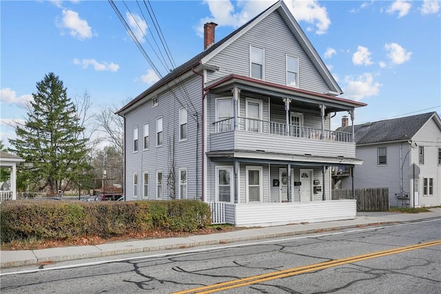 view of front of property with a balcony, a chimney, and fence