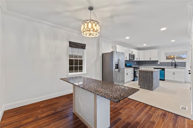 kitchen with tasteful backsplash, a kitchen island, ornamental molding, light wood-style flooring, and stainless steel appliances