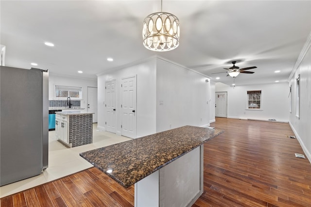 kitchen featuring a kitchen island, ornamental molding, freestanding refrigerator, light wood-style floors, and a sink