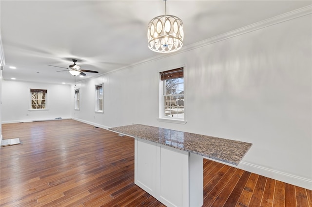 unfurnished living room with ornamental molding, ceiling fan with notable chandelier, baseboards, and dark wood-style flooring