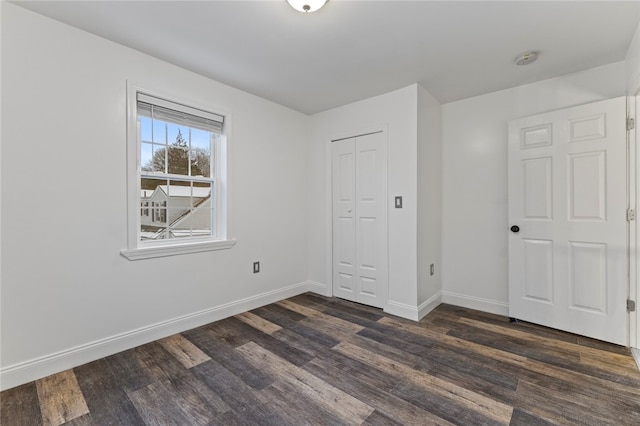 unfurnished bedroom featuring dark wood-style floors, a closet, and baseboards