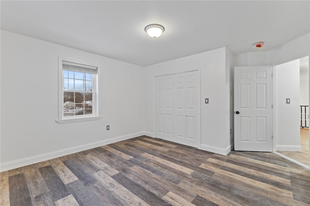 unfurnished bedroom with dark wood-style floors, baseboards, and a closet