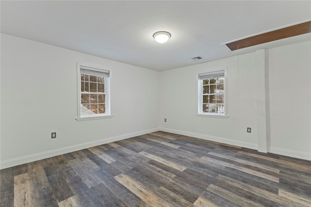 empty room with attic access, dark wood-style floors, baseboards, and visible vents