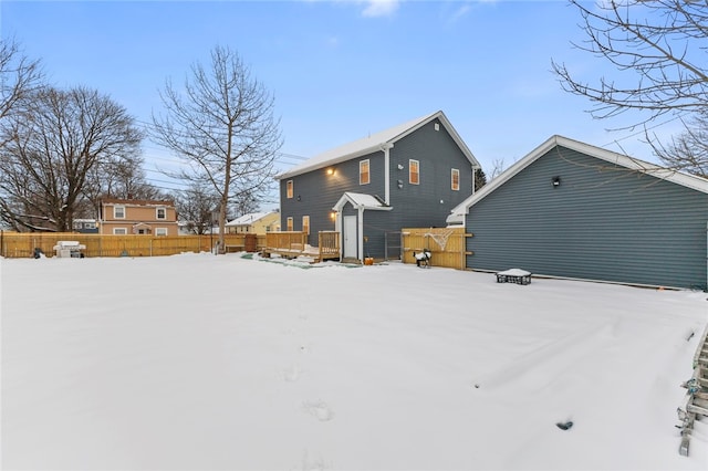 snow covered rear of property with a deck and fence