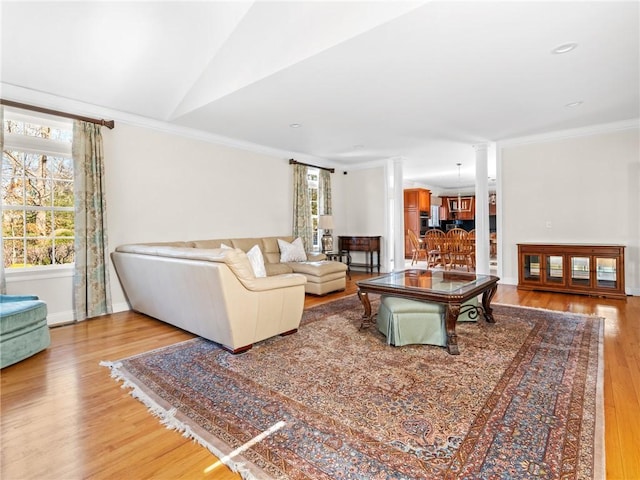 living area featuring ornamental molding, light wood finished floors, baseboards, vaulted ceiling, and ornate columns