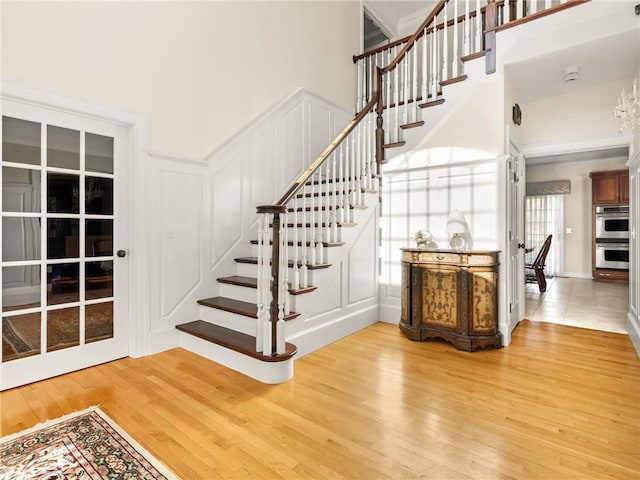 stairway featuring crown molding, a decorative wall, wood finished floors, and a towering ceiling