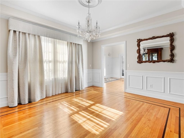 unfurnished room featuring a chandelier, a wainscoted wall, crown molding, and wood finished floors