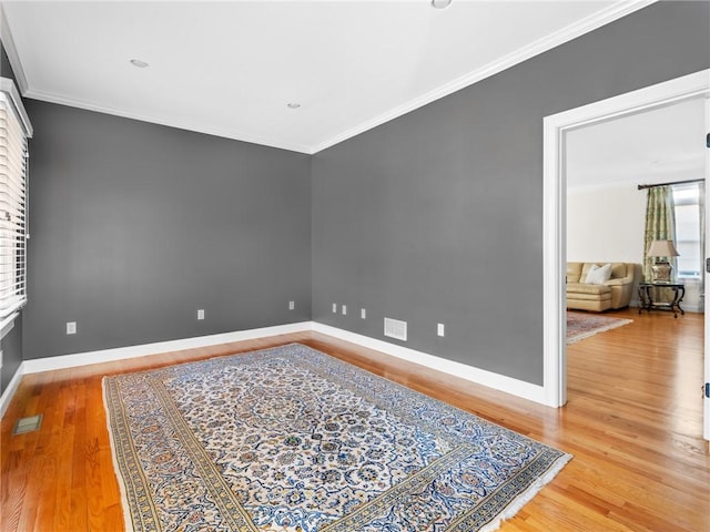 spare room with crown molding, wood finished floors, visible vents, and baseboards