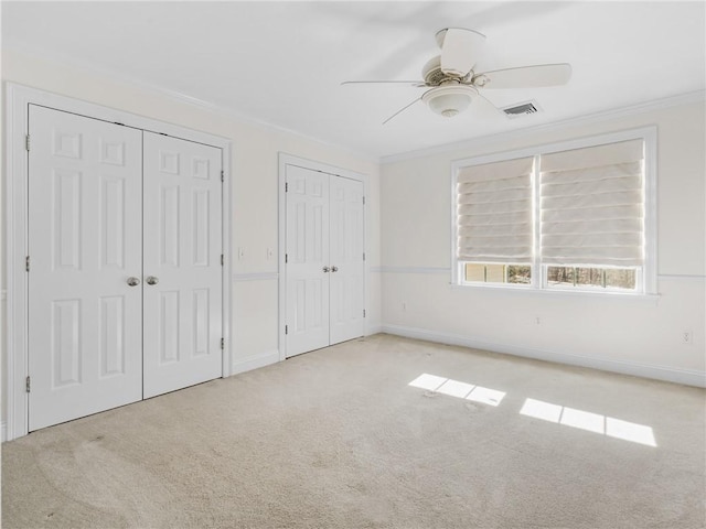 unfurnished bedroom with two closets, crown molding, baseboards, ceiling fan, and carpet