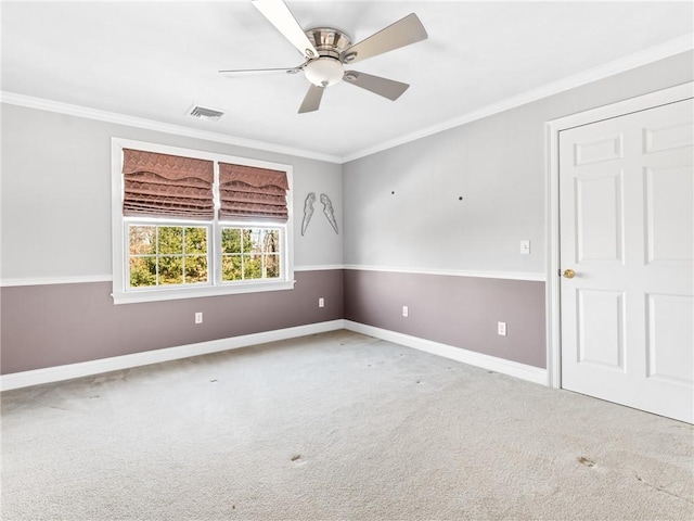 carpeted empty room with visible vents, baseboards, ceiling fan, and crown molding