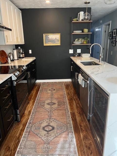 kitchen with dark cabinetry, a peninsula, a sink, black range with electric cooktop, and white cabinetry