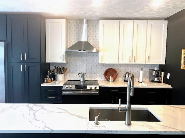 kitchen with wall chimney range hood, decorative backsplash, white cabinets, stainless steel appliances, and a sink