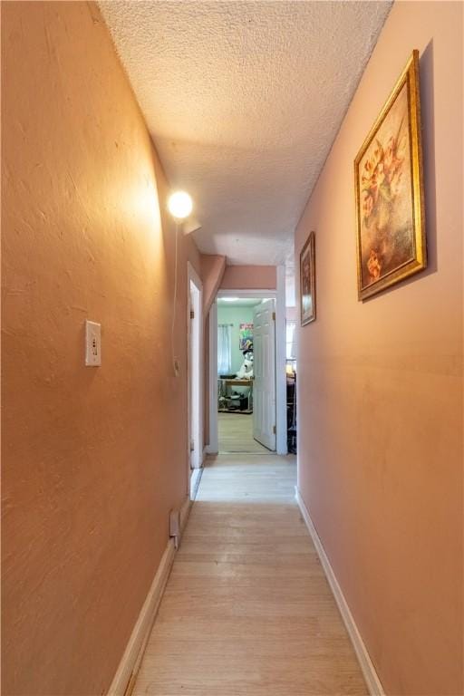 hall featuring a textured ceiling, light wood-type flooring, and baseboards