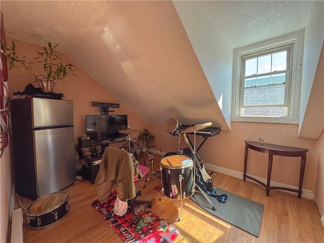 interior space with vaulted ceiling, a textured ceiling, baseboards, and wood finished floors