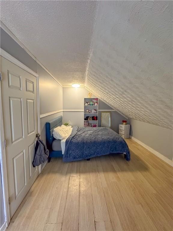 bedroom featuring baseboards, a textured ceiling, lofted ceiling, and wood finished floors