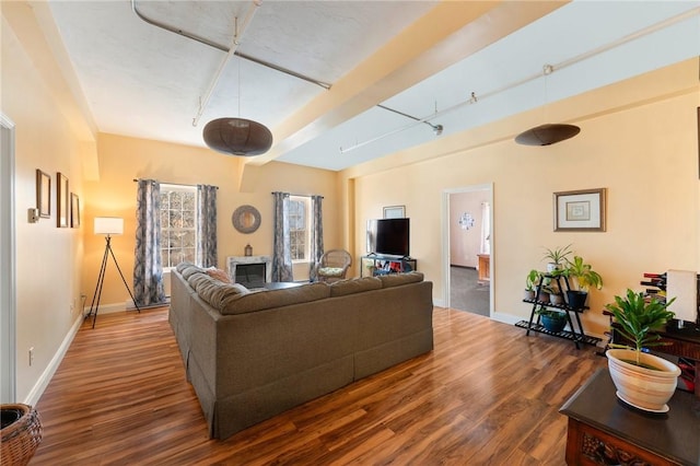 living room featuring beamed ceiling, rail lighting, baseboards, and wood finished floors