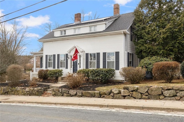 view of front of house with roof mounted solar panels, a chimney, and a shingled roof