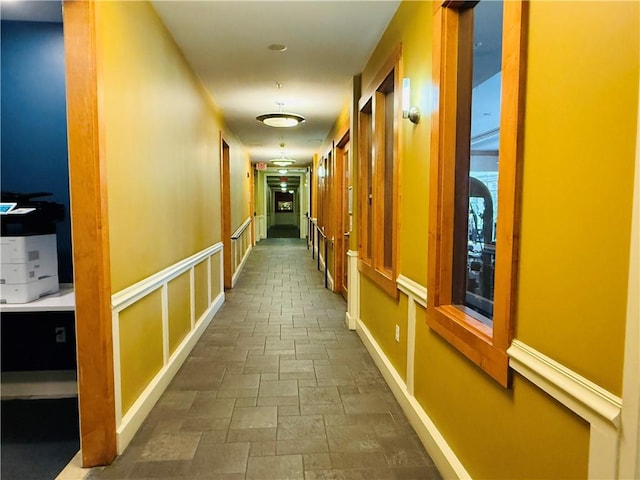 hall with a wainscoted wall, stone finish flooring, and baseboards