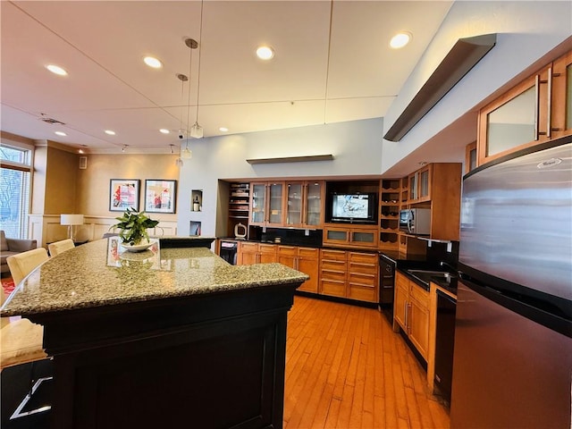 kitchen with brown cabinetry, a spacious island, glass insert cabinets, light wood-style floors, and appliances with stainless steel finishes